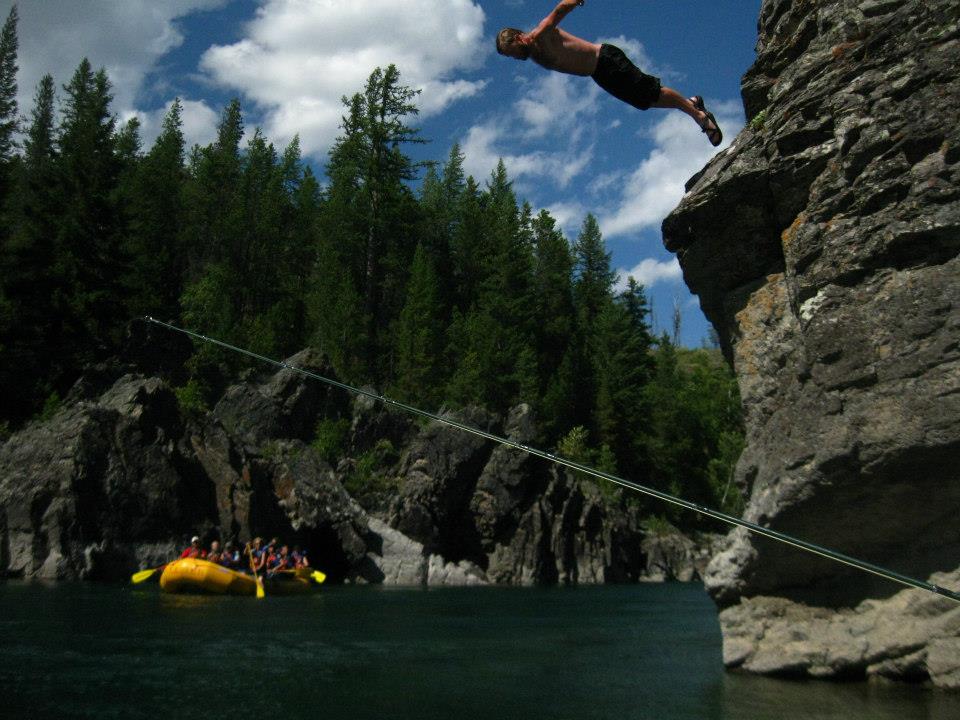 A leap from a rocky cliff above a forest-lined river